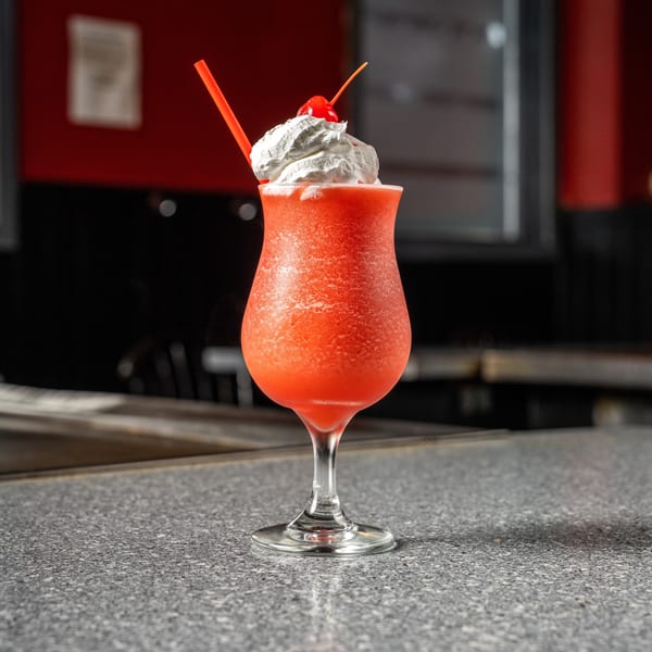 A vibrant red frozen drink with whipped cream, a cherry, and a straw on a speckled countertop.