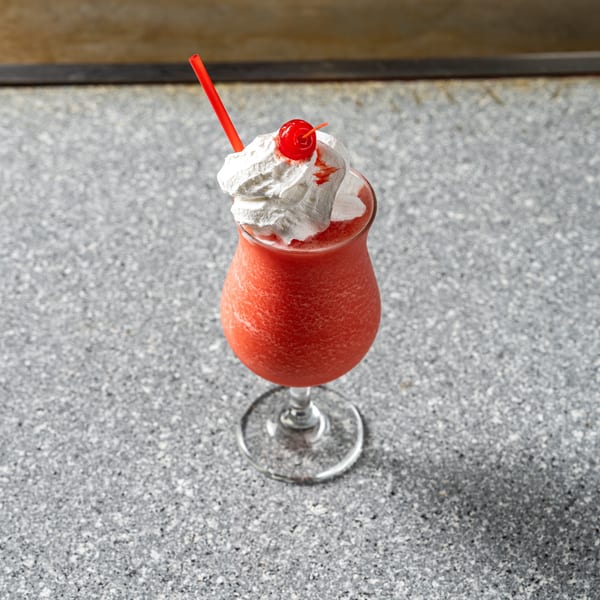 A red frozen drink with whipped cream, a cherry, and a red straw on a speckled gray surface.