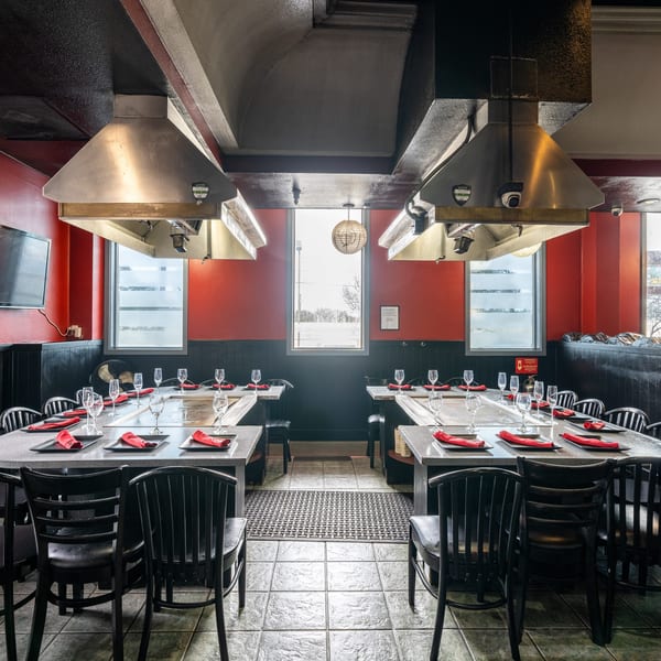 Empty hibachi dining room with red walls, black chairs, and long tables set with red napkins.