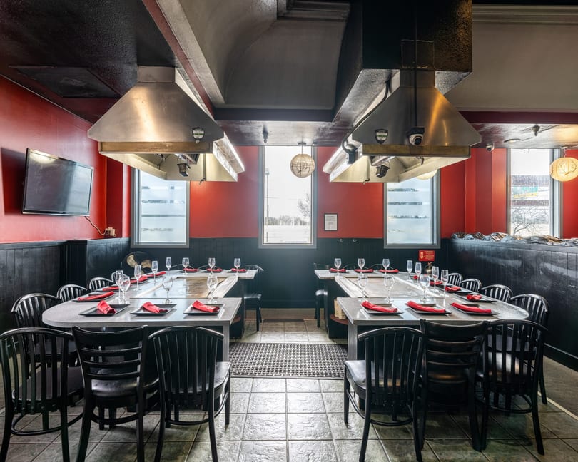 Empty hibachi dining room with red walls, black chairs, and long tables set with red napkins.