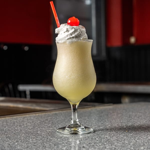 A frozen cocktail with whipped cream, a cherry, and a red straw sits on a speckled gray bar.