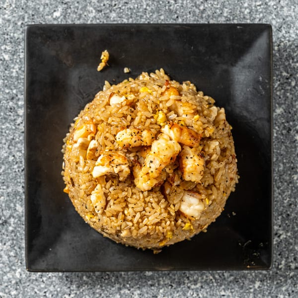 Top-down view of shrimp fried rice with black pepper, served on a black square plate.
