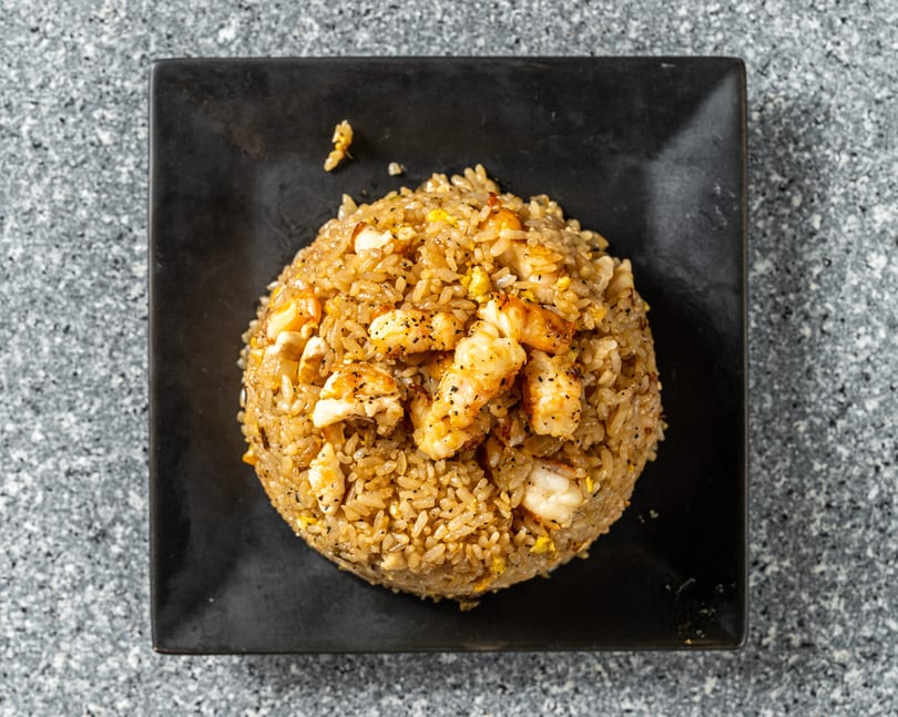 Top-down view of shrimp fried rice with black pepper, served on a black square plate.