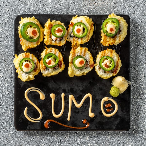 Eight fried sushi rolls topped with jalapeño, sauce, and a red dot, with "SUMO" written in sauce.