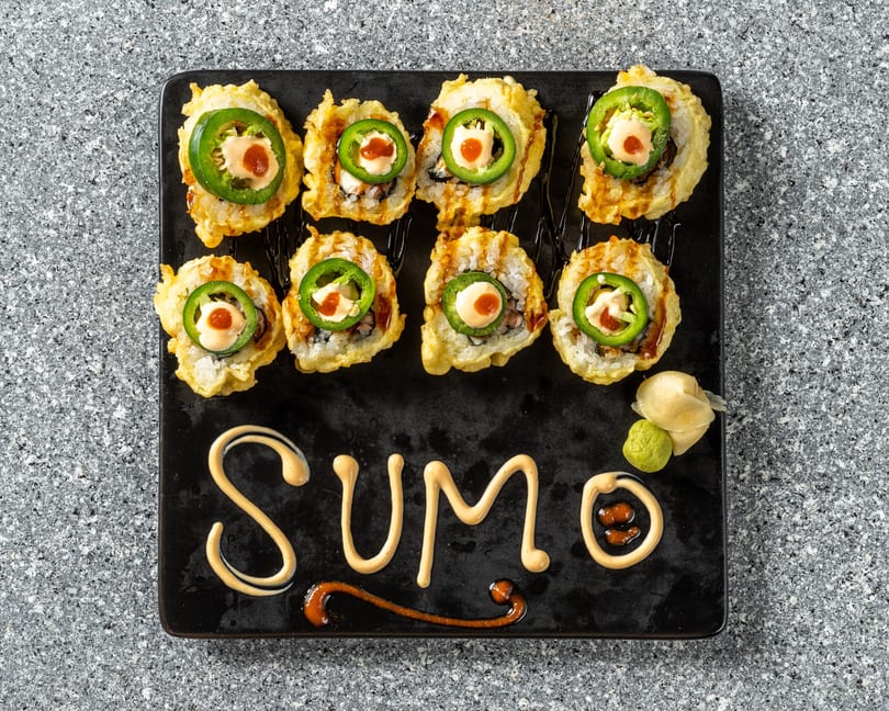 Eight fried sushi rolls topped with jalapeño, sauce, and a red dot, with "SUMO" written in sauce.