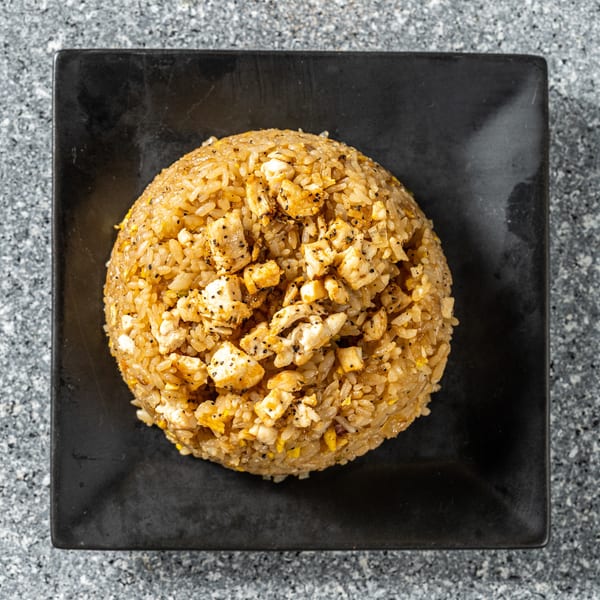 Top-down view of a dome-shaped chicken fried rice dish on a black square plate.