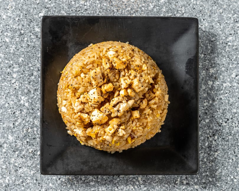 Top-down view of a dome-shaped chicken fried rice dish on a black square plate.