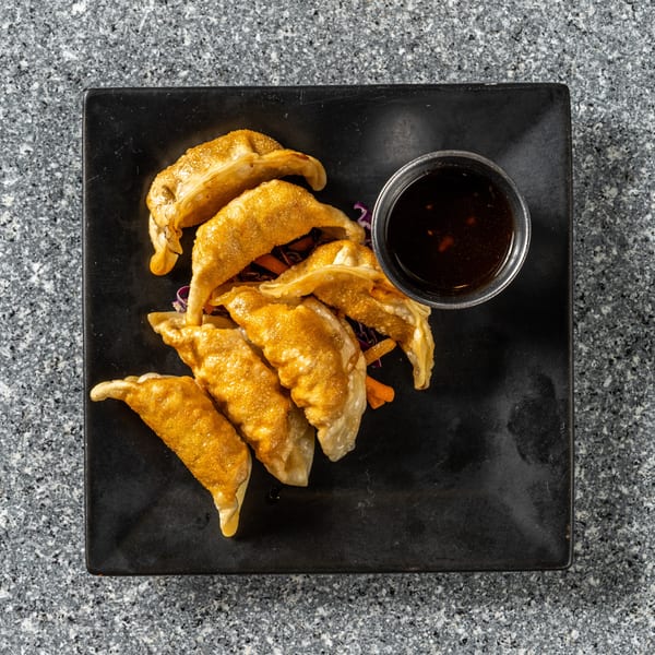 Golden-brown fried dumplings with a side of dark dipping sauce on a black rectangular plate.