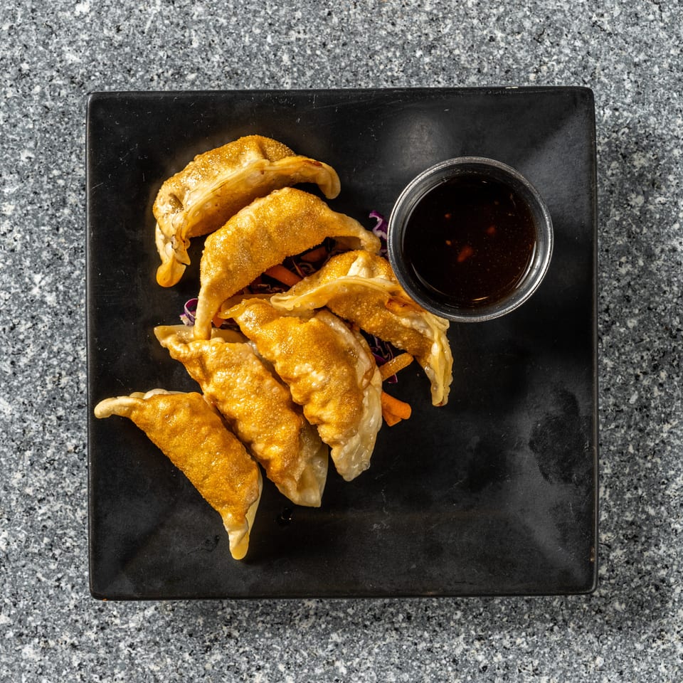 Golden-brown fried dumplings with a side of dark dipping sauce on a black rectangular plate.