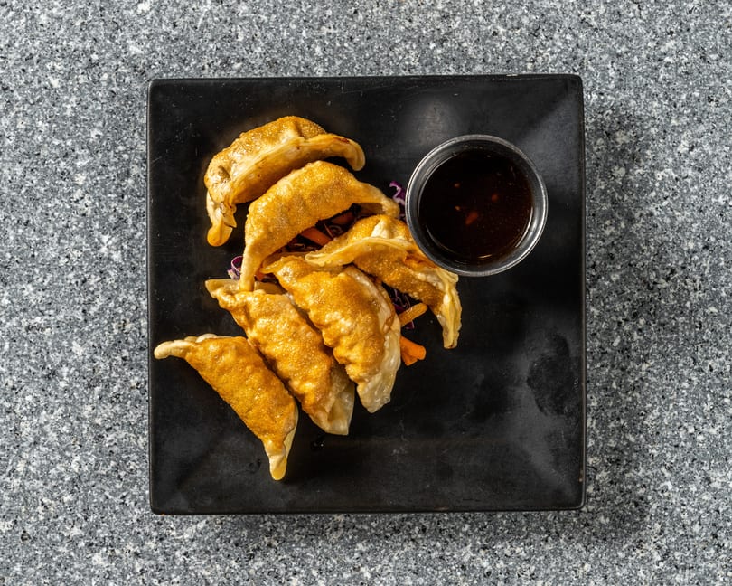 Golden-brown fried dumplings with a side of dark dipping sauce on a black rectangular plate.