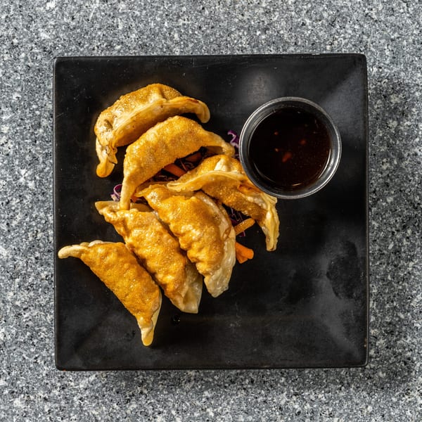 Golden-brown fried dumplings with a side of dark dipping sauce on a black rectangular plate.