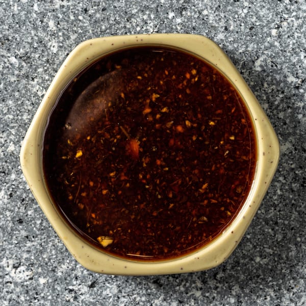 Overhead view of a hexagonal bowl filled with dark, spicy chili oil on a speckled gray surface.