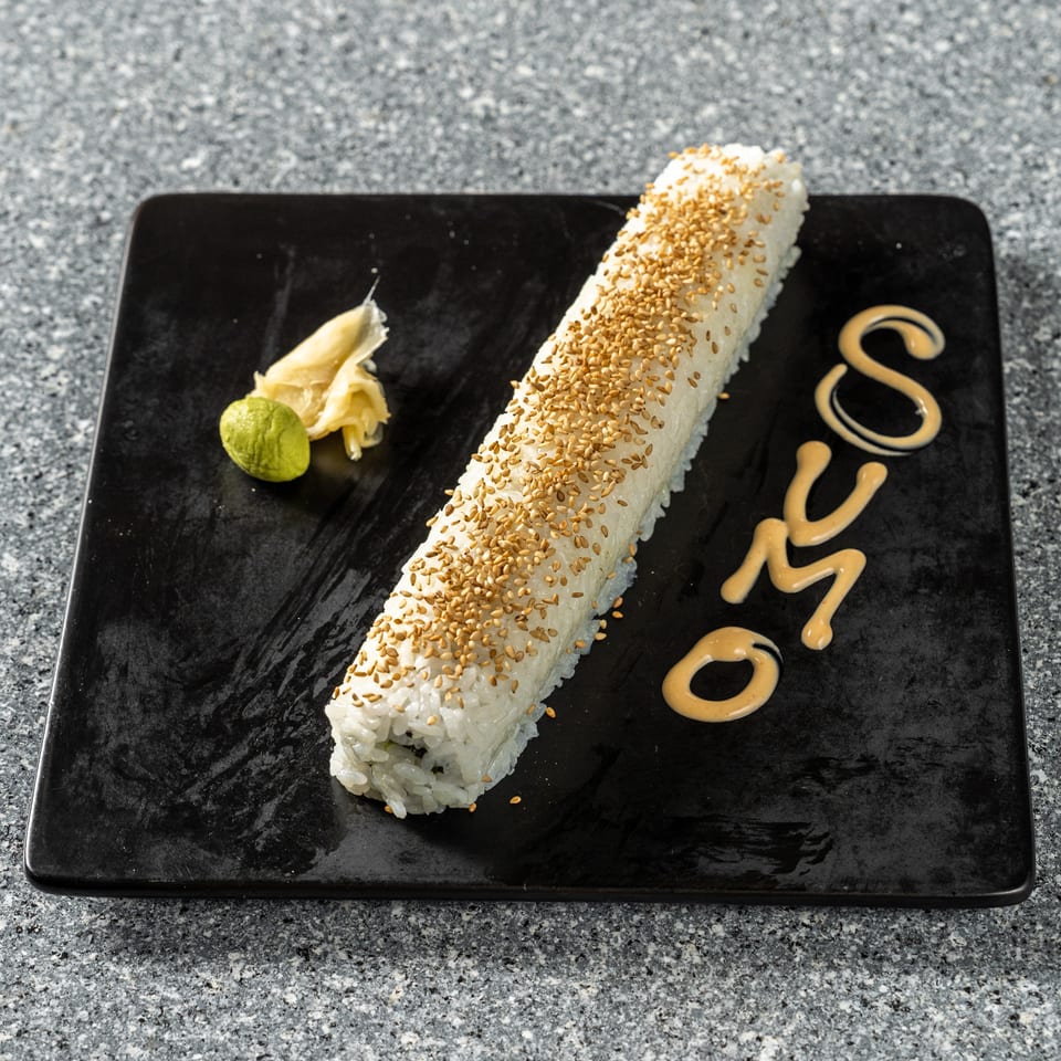 Long sushi roll topped with sesame seeds, with wasabi, ginger, and "SUMO" written in sauce.