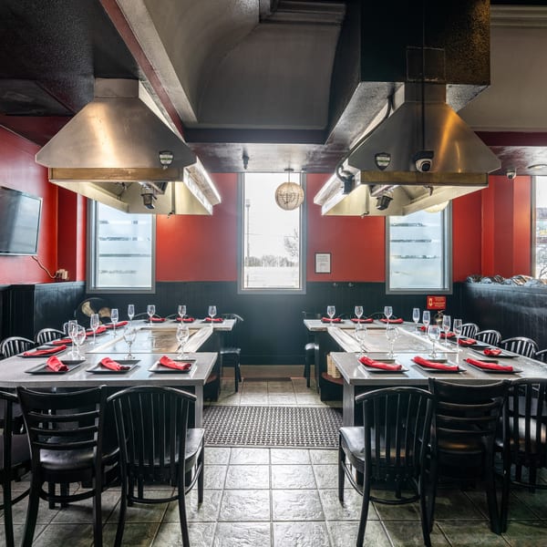Empty hibachi dining room with red walls, black chairs, and long tables set with red napkins.