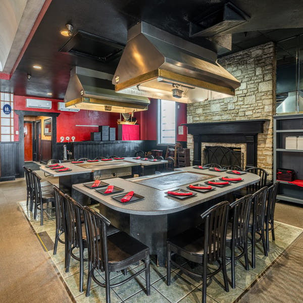 Empty hibachi restaurant dining room with red walls, black chairs, and cooking stations with red napkins.