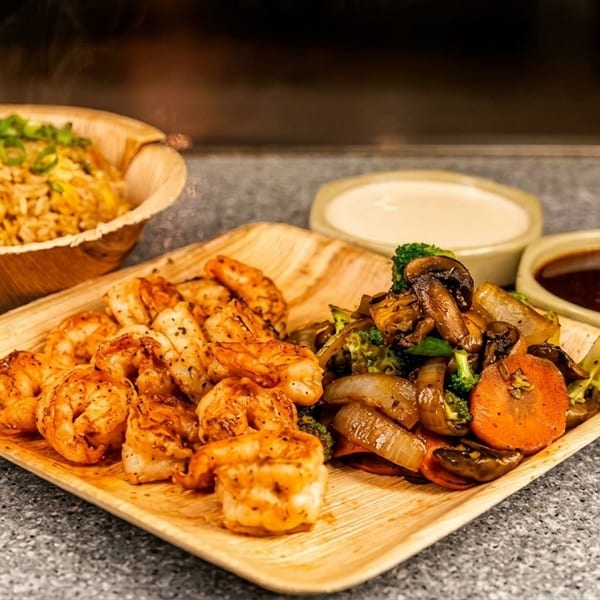 Shrimp, mixed vegetables, and fried rice in bamboo bowls, with two dipping sauces.