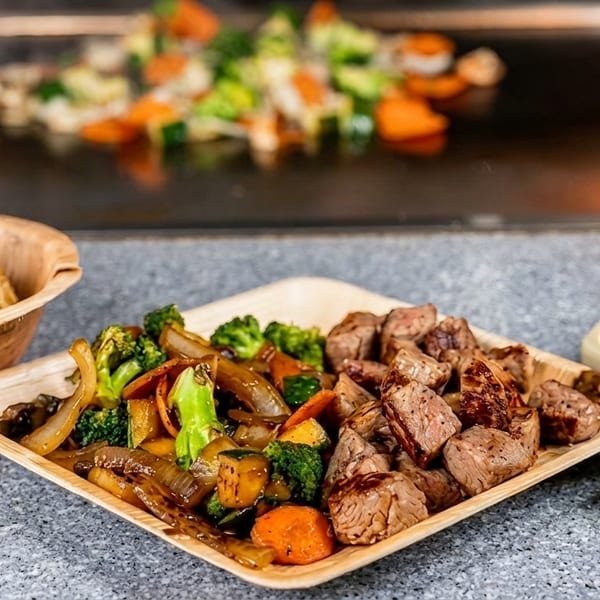 Hibachi steak, vegetables, and fried rice with two dipping sauces, cooking on a flaming grill.