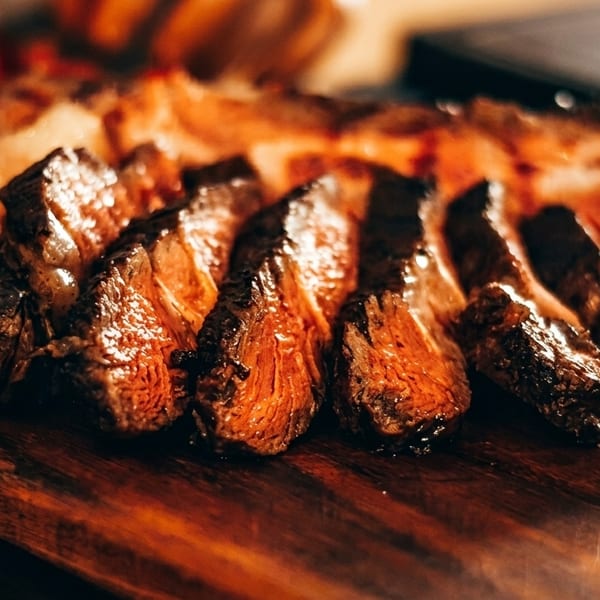 Close-up of perfectly cooked, sliced steak with a charred crust on a wooden cutting board.