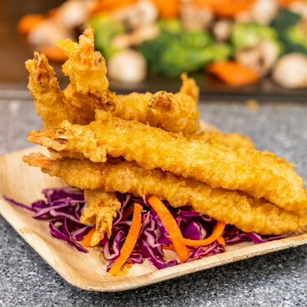 Crispy fried shrimp tempura on a wooden plate with shredded red cabbage and carrots.
